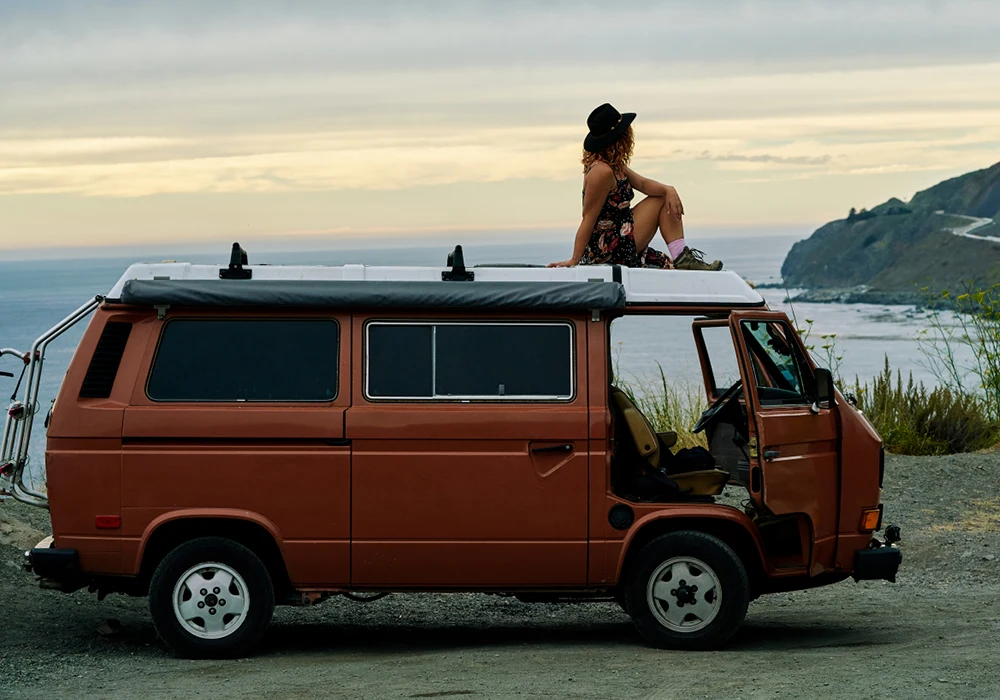 Woman sitting on roof of camper van looking at the ocean