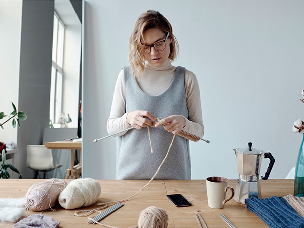 Woman stand beside a table in her home working on a knitting project