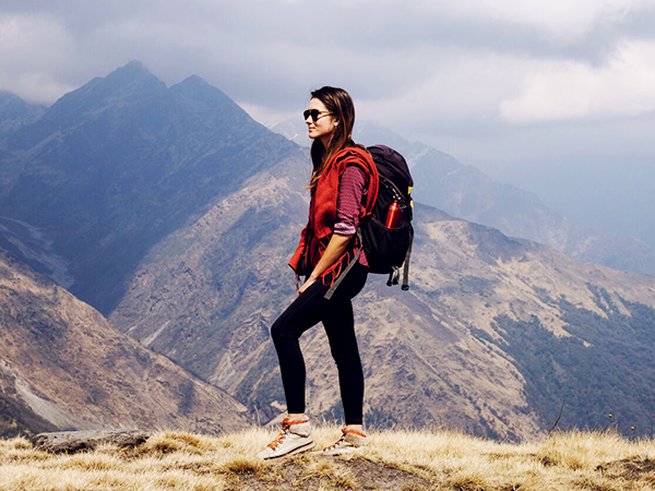 Woman with hiking gear on stands looking out over mountain scenery. 