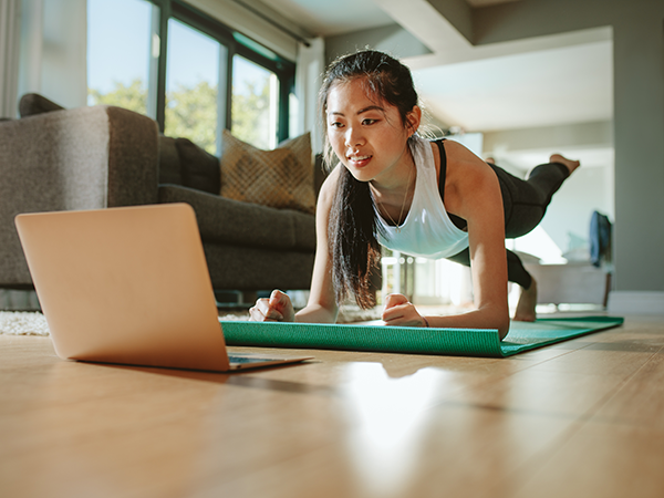 Young woman doing yoga on a mat while looking at laptop