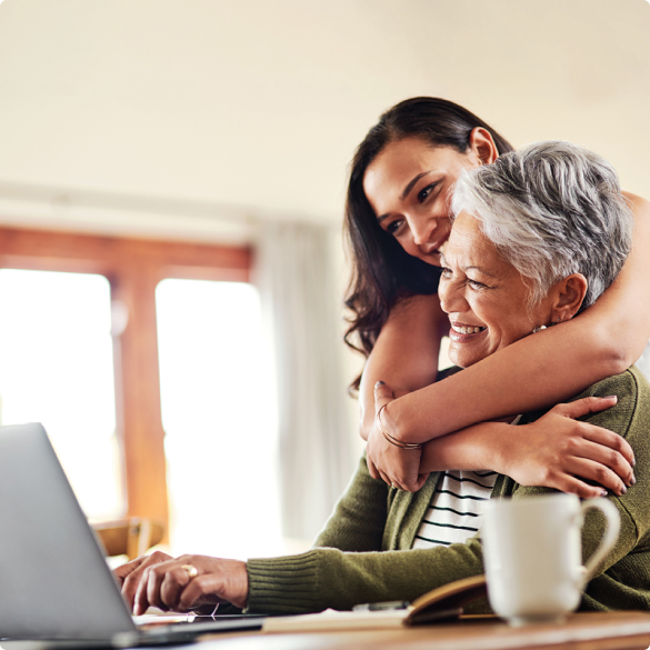 Older woman working on laptop while adult daughter gives hug from behind